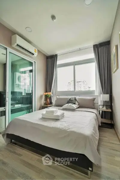 Modern bedroom with large window and city view, featuring cozy bed and stylish decor.