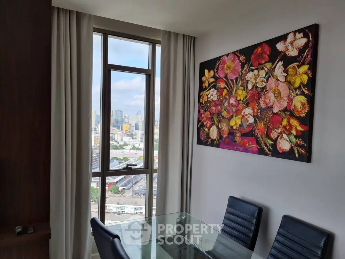 Modern dining area with city view and vibrant floral artwork, featuring sleek glass table and leather chairs.