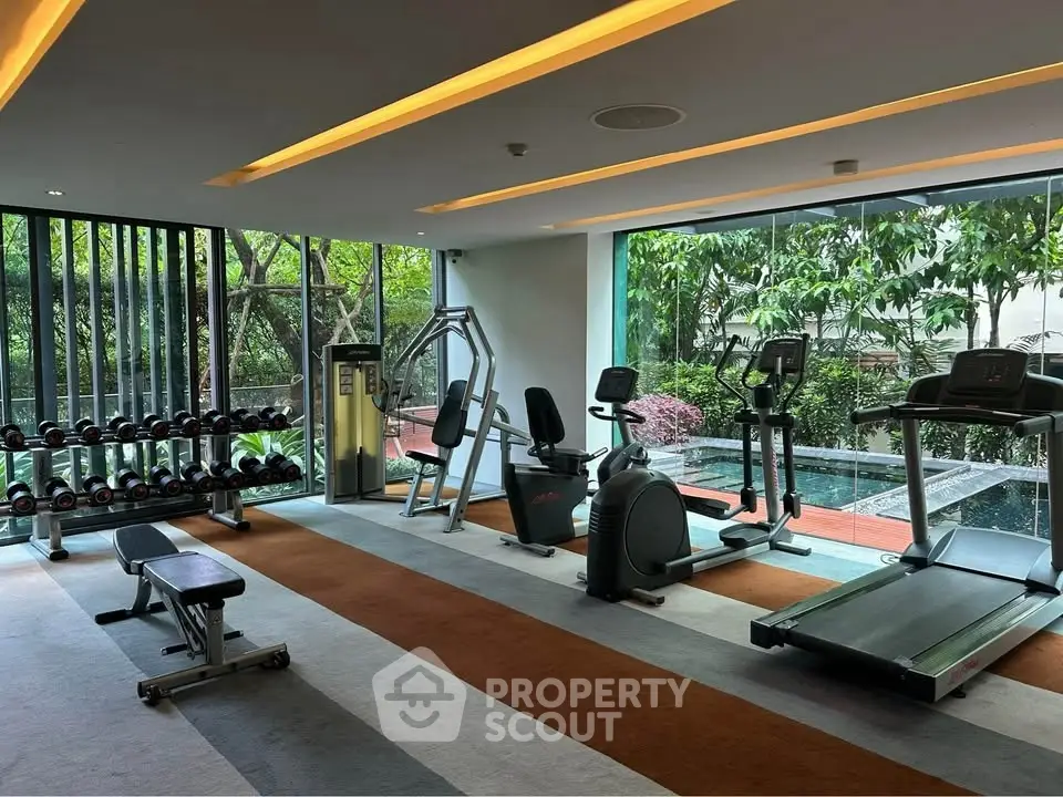 Modern gym with exercise equipment and large windows overlooking a garden view.