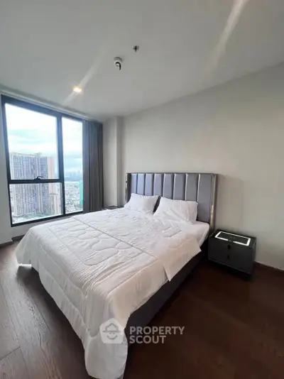 Modern bedroom with large window and city view in high-rise apartment.
