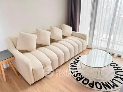 Modern living room with stylish beige sofa and unique alphabet rug near a glass coffee table.