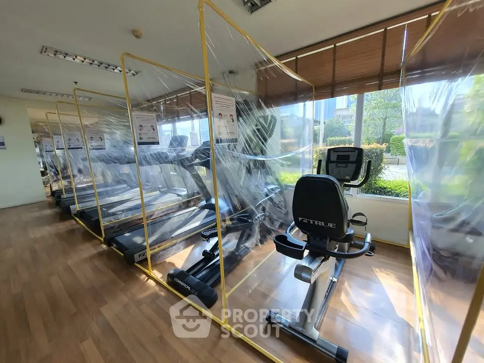 Modern gym with exercise equipment and safety partitions in a bright, sunlit room.