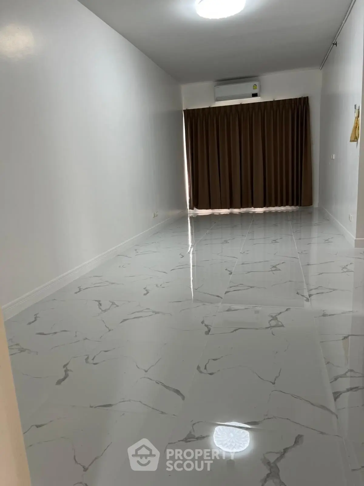 Spacious empty room with elegant marble flooring and large window with curtains.