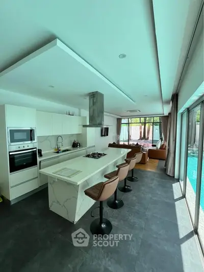 Luxurious open-layout kitchen with island and poolside view, featuring modern appliances and stylish bar seating.