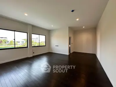 Spacious empty room with dark wood flooring and large windows offering natural light and garden views.