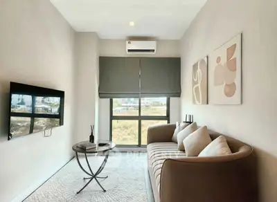 Modern living room with sleek sofa, wall-mounted TV, and large window offering natural light.
