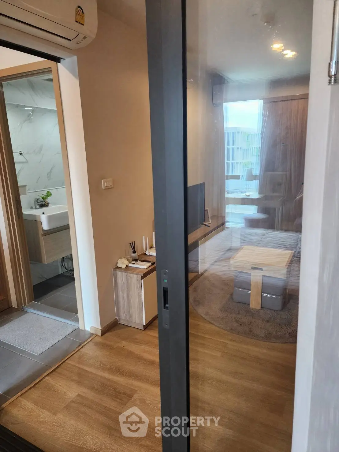 Modern apartment interior with open living room and bathroom view, featuring sleek wooden flooring and contemporary decor.
