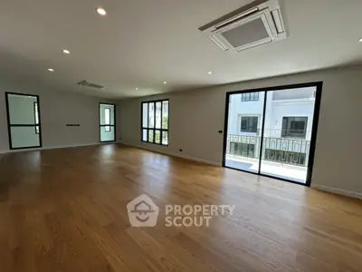 Spacious modern living room with wooden flooring and large windows for natural light.