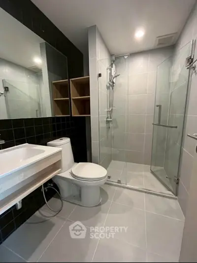 Modern bathroom with glass shower, sleek fixtures, and large mirror in contemporary apartment.
