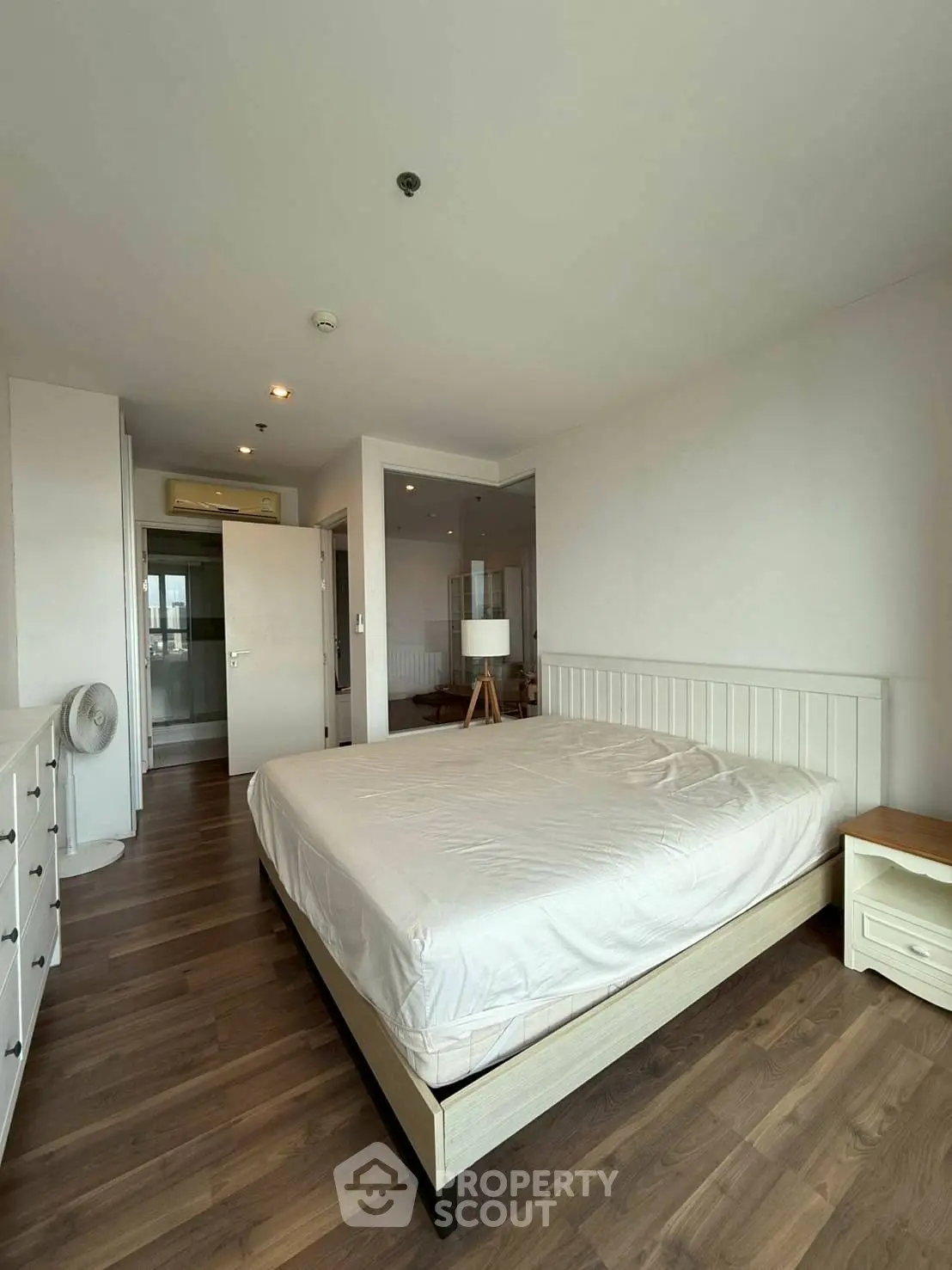 Spacious bedroom with wooden flooring and modern furnishings in a bright apartment.