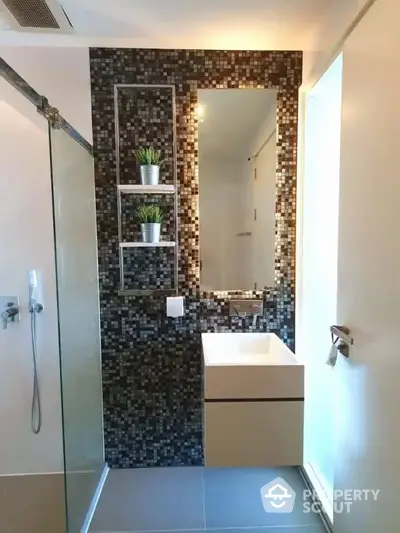 Modern bathroom with sleek design, featuring mosaic tiles, glass shower, and stylish vanity with mirror and plant decor.