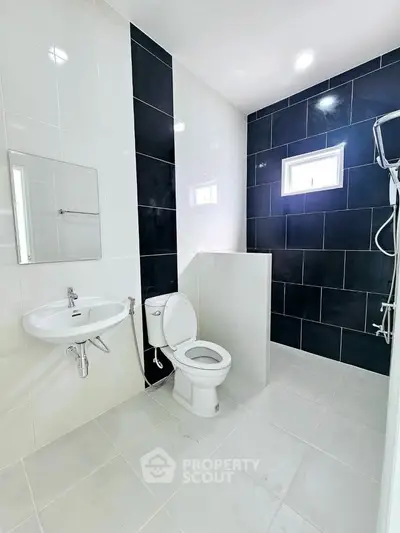Modern bathroom with sleek black and white tiles, featuring a toilet, sink, and shower area.