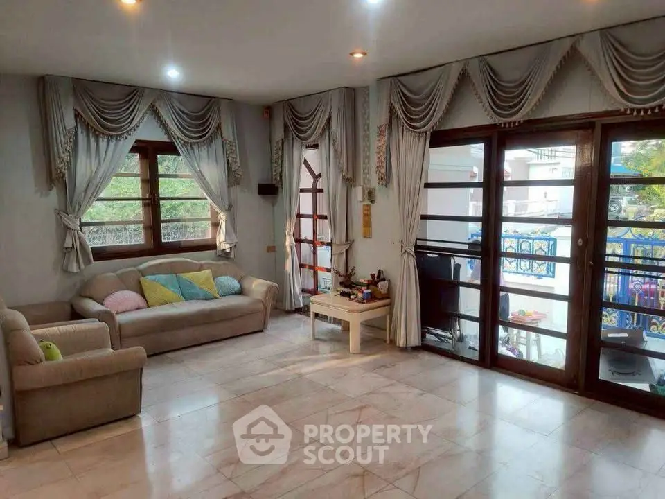 Spacious living room with elegant drapes and large windows offering natural light and garden view.