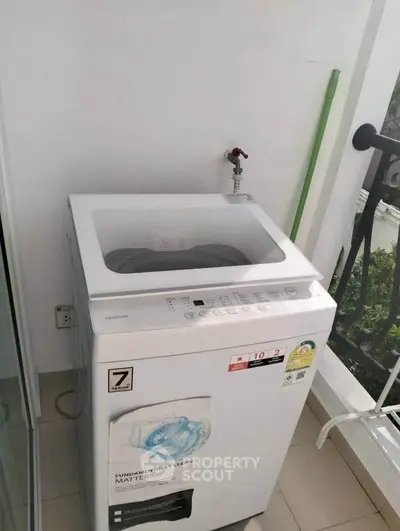 Modern washing machine on a balcony with a sleek railing and greenery view.