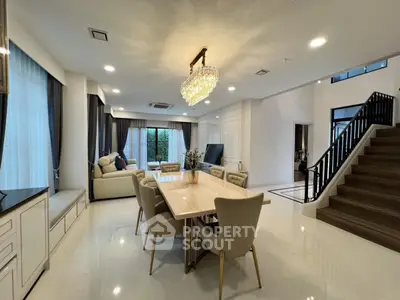 Luxurious open-plan living and dining area with elegant chandelier and modern staircase.