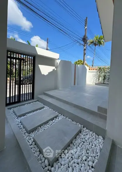 Modern minimalist entrance with stone pathway and sleek gate under clear blue sky.