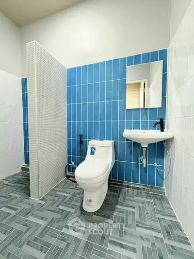 Modern bathroom with blue and white tiles, featuring a sleek toilet and wall-mounted sink.