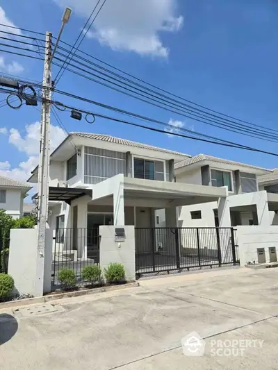 Modern two-story house with gated driveway and contemporary design under clear blue sky.