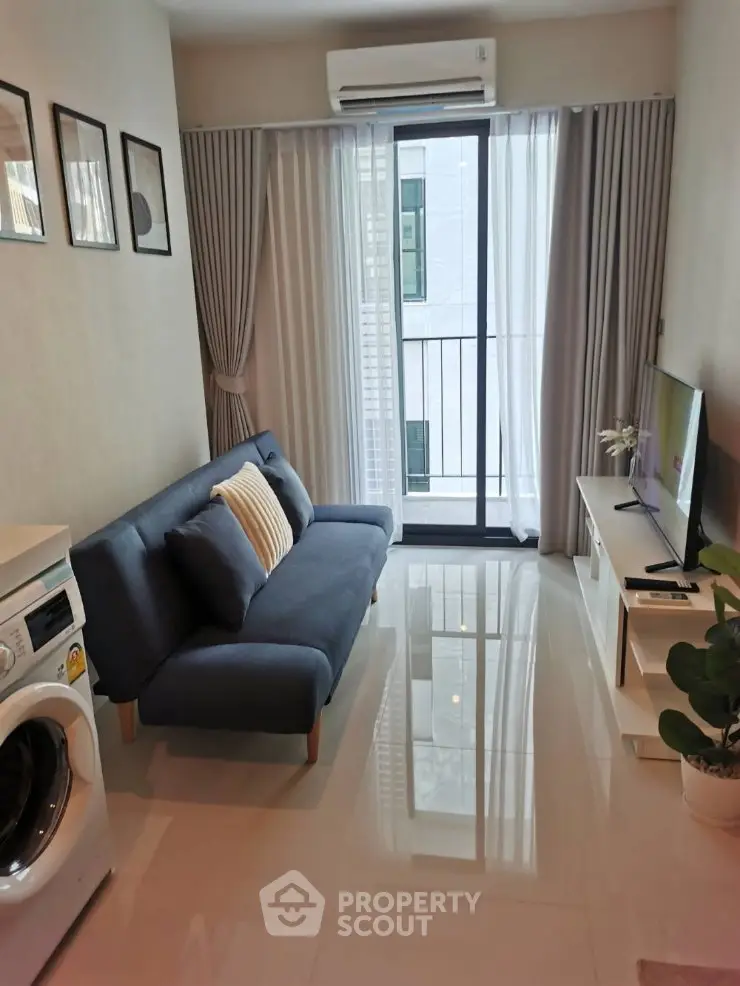 Modern living room with sleek sofa, TV, and washing machine near balcony in stylish apartment.
