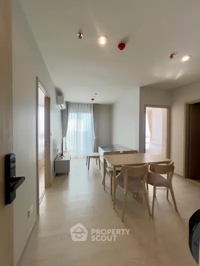 Modern living room with dining area and natural light, featuring minimalist furniture and wooden flooring.