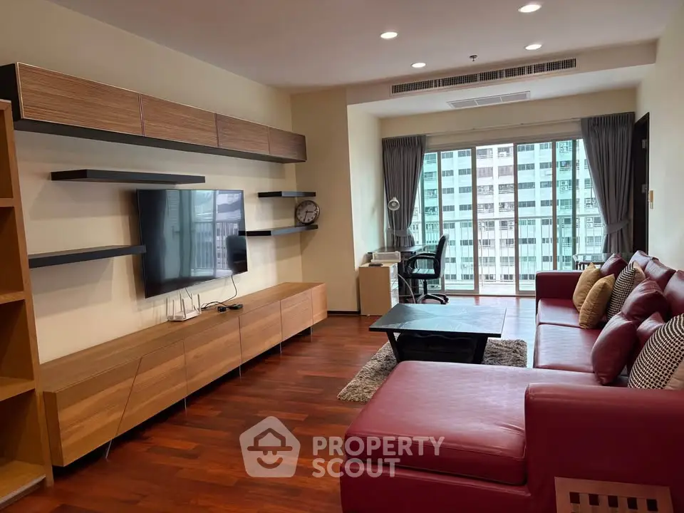 Spacious modern living room with red leather sofa and large TV, featuring city view from window.
