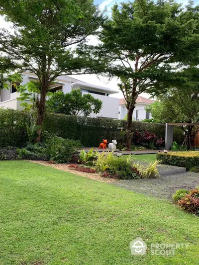 Lush green garden with manicured lawns and vibrant flower beds in front of modern white residential buildings, offering a serene and luxurious living environment.