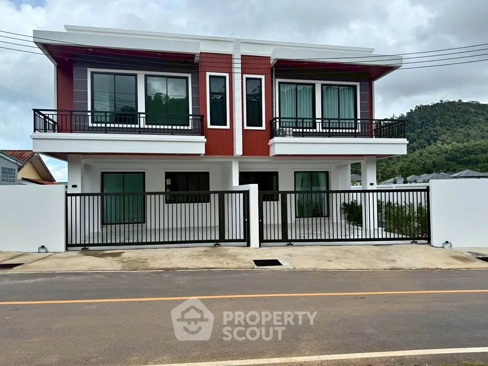 Modern two-story red and white house with gated entrance and mountain backdrop.