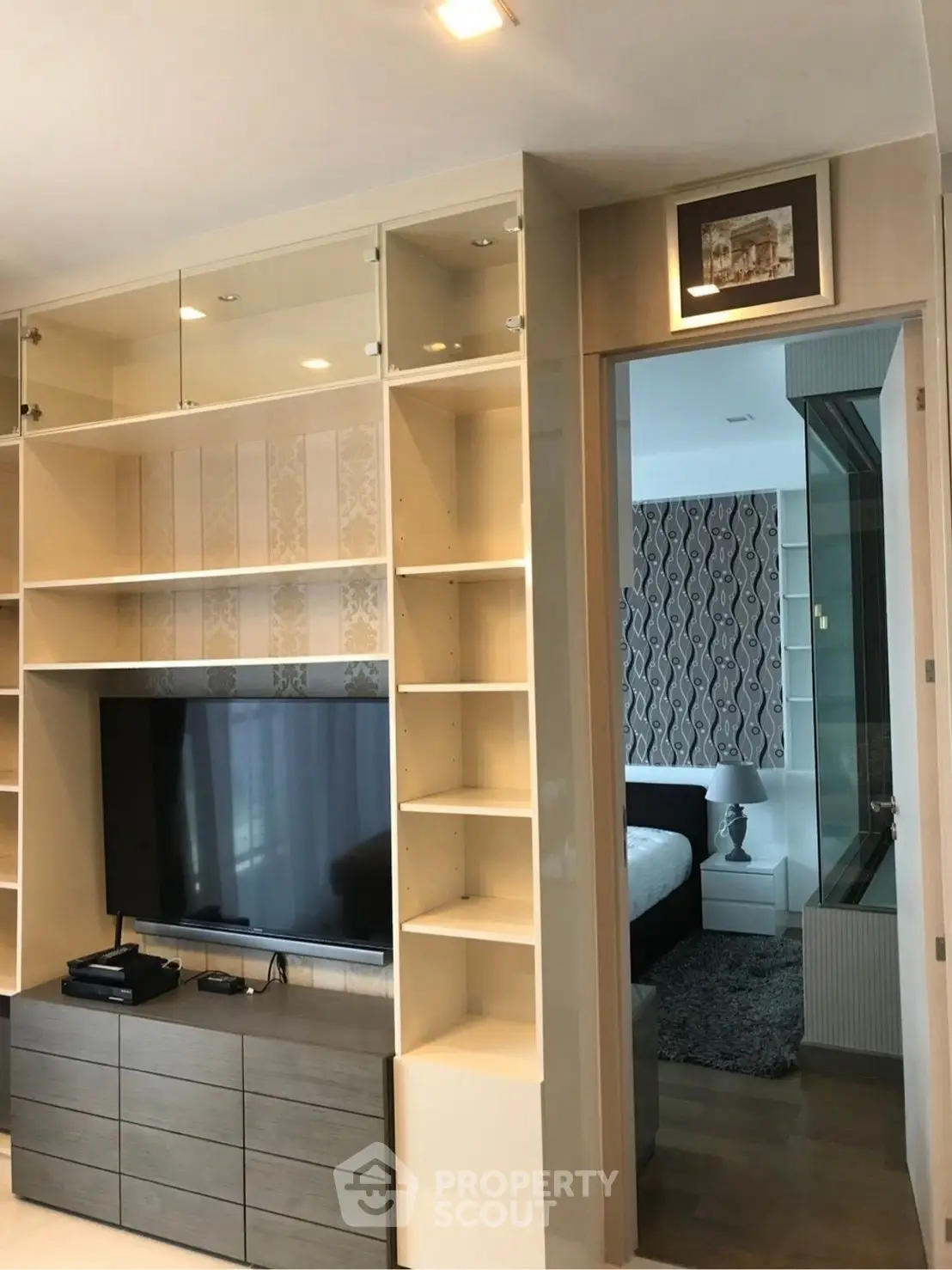 Modern living room with built-in shelves and TV, leading to a stylish bedroom.
