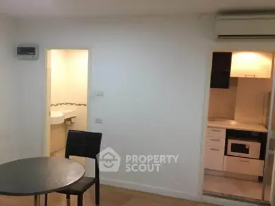 Compact apartment interior with dining area, visible kitchen, and bathroom entrance.