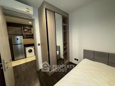 Modern bedroom with sleek wardrobe and view into kitchen with appliances