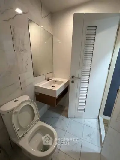 Modern bathroom with sleek fixtures and marble tiles, featuring a compact design and elegant finishes.