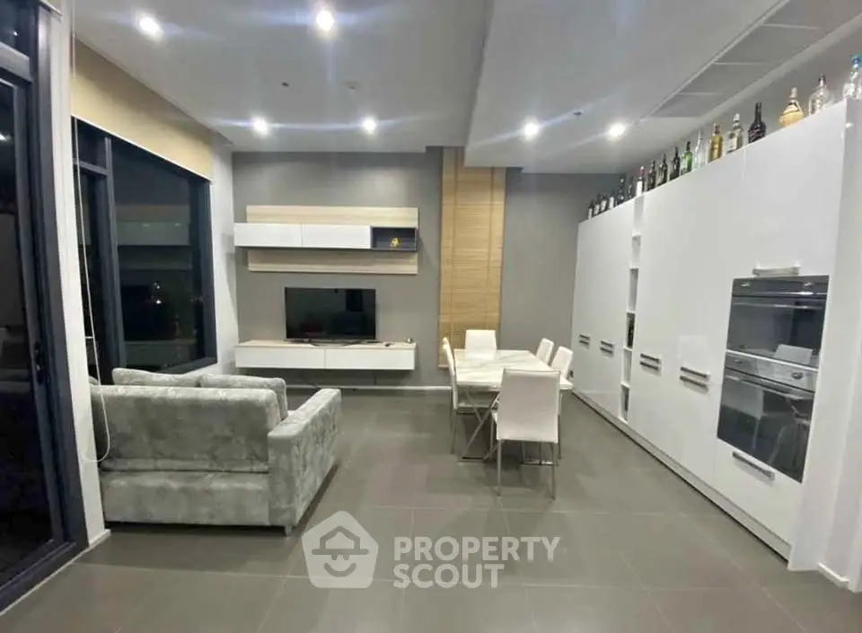 Modern open-plan living room with sleek kitchen and dining area, featuring stylish furniture and ambient lighting.