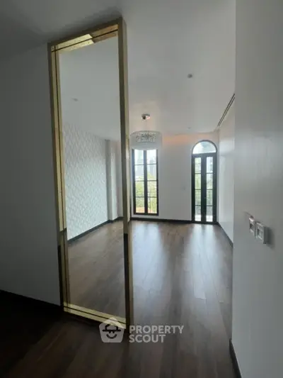 Elegant spacious living room with rich hardwood floors, large windows offering ample natural light, and a stylish chandelier, perfect for modern living.