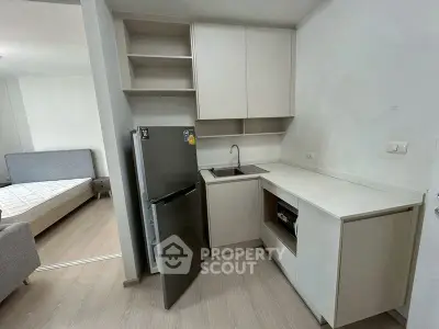 Modern compact kitchen with open fridge and adjacent bedroom view