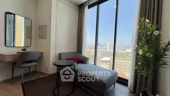 Modern living room with floor-to-ceiling windows and city view, featuring a sleek chaise lounge and stylish decor.