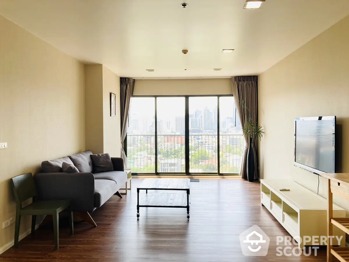 Spacious living room with gleaming hardwood floors, modern furniture, and abundant natural light from large windows offering a city view.