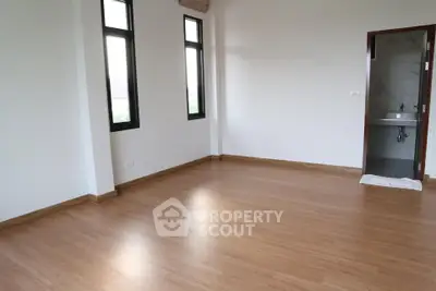 Spacious empty room with wooden flooring and natural light from large windows.