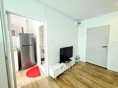 Modern living room with TV and open kitchen view, featuring sleek wooden flooring and minimalist design.