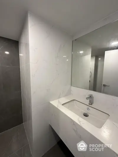 Modern bathroom with sleek marble sink and large mirror, featuring elegant gray and white tile design.