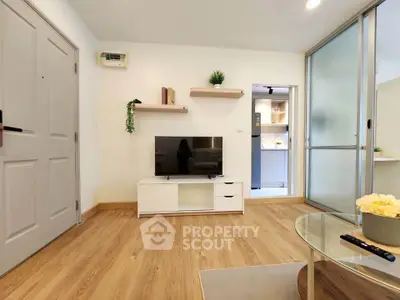 Modern living room with wooden flooring and sleek TV setup, adjacent to a stylish kitchen.