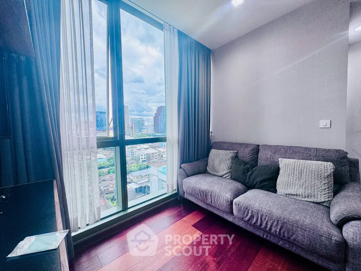 Modern living room with large window offering stunning city view, featuring a cozy gray sofa and elegant wooden flooring.