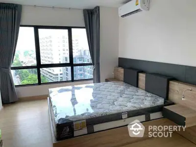 Modern bedroom with large window and city view, featuring a stylish bed and air conditioning.