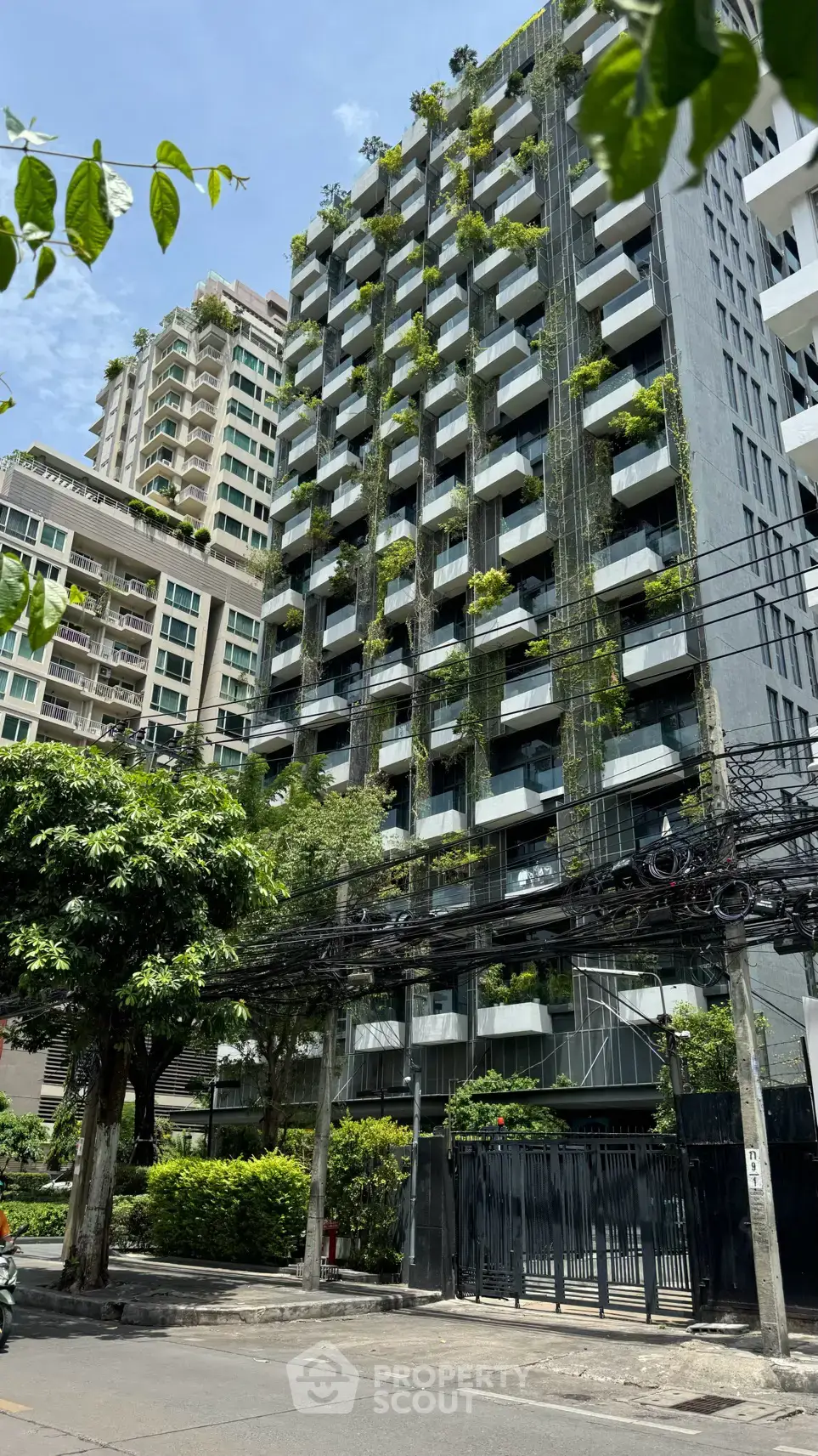 Modern high-rise building with lush green balconies and urban surroundings.
