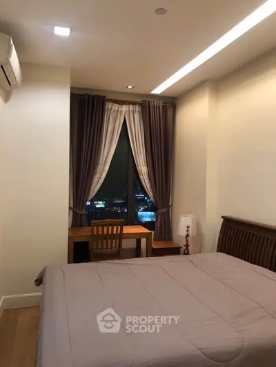 Cozy bedroom with city view, featuring a wooden bed and desk, ideal for urban living.