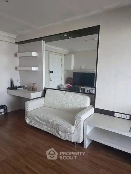 Modern living room with sleek furniture and wooden flooring, featuring a stylish sofa and wall-mounted shelves.
