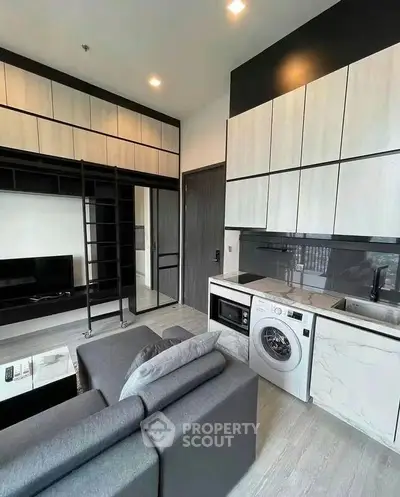 Modern living room with integrated kitchen and washing machine, featuring sleek cabinetry and a cozy sofa.