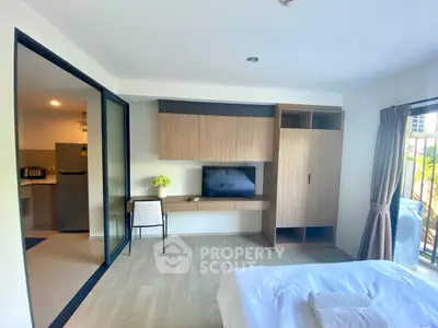 Modern bedroom with TV and sliding glass doors leading to kitchen area, featuring stylish wooden cabinetry.