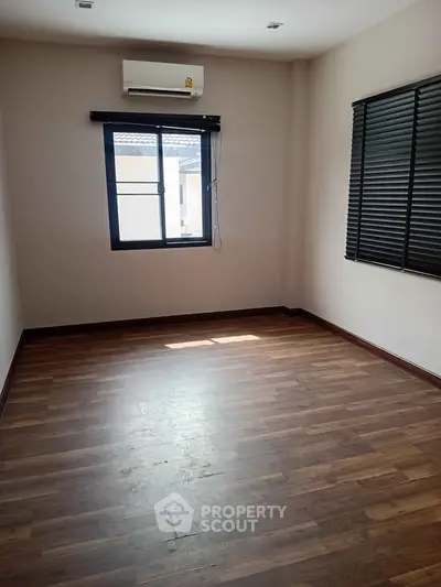 Spacious empty room with wooden flooring and large window, perfect for customization.