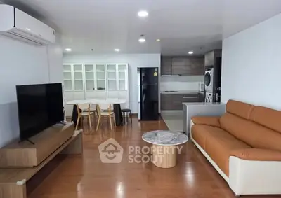 Modern living room with open kitchen, featuring sleek furniture and hardwood floors.