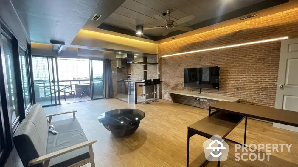 Spacious modern living room with exposed brick wall, sleek furnishings, and a large balcony offering an abundance of natural light.